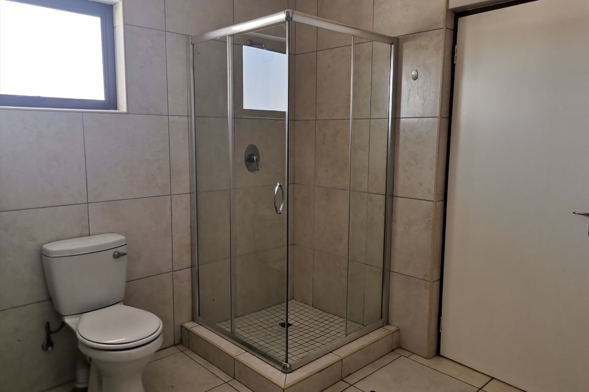 A functional bathroom featuring a corner shower enclosure, toilet, and neutral wall and floor tiling.