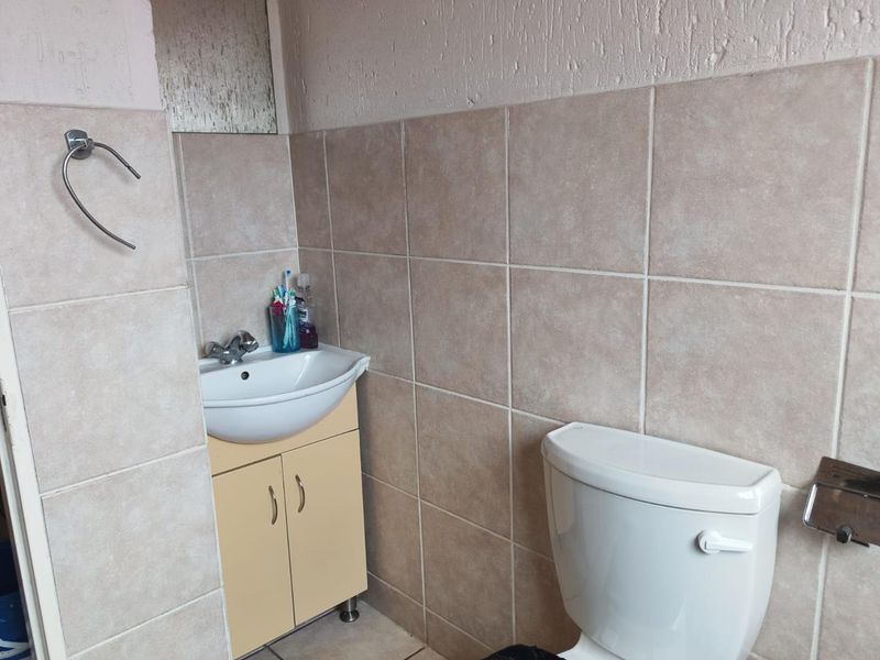 A compact bathroom featuring a vanity cabinet with basin, toilet, and neutral wall tiling. The space would benefit from modern updates to finishes.