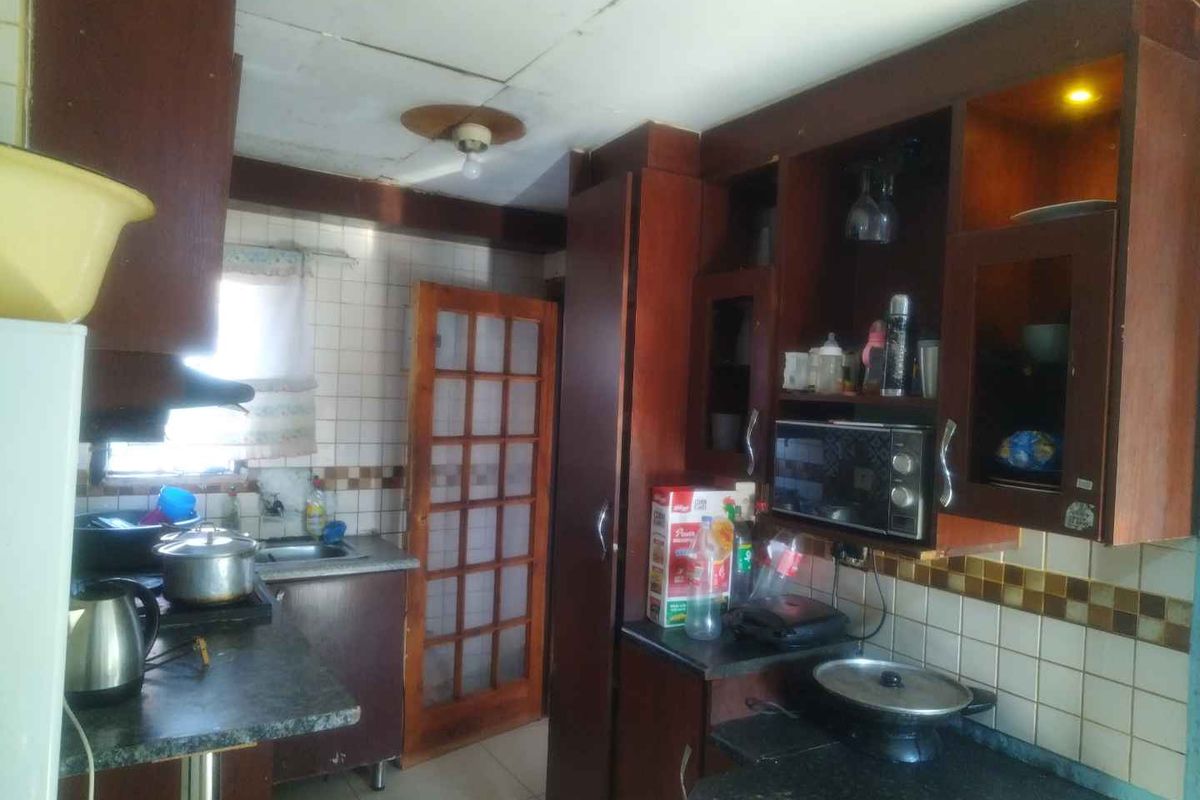 A dated kitchen featuring dark wood cabinetry, tiled backsplash, and laminate countertops, requiring modernization to improve functionality and aesthetic appeal.