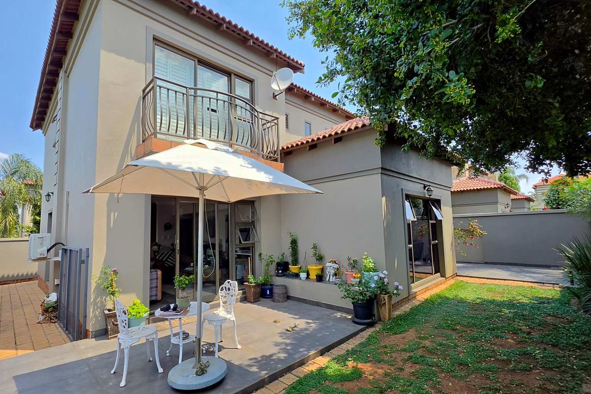 Rear view of the townhouse featuring a paved patio area, a first-floor balcony with metal railings, and a private garden space.