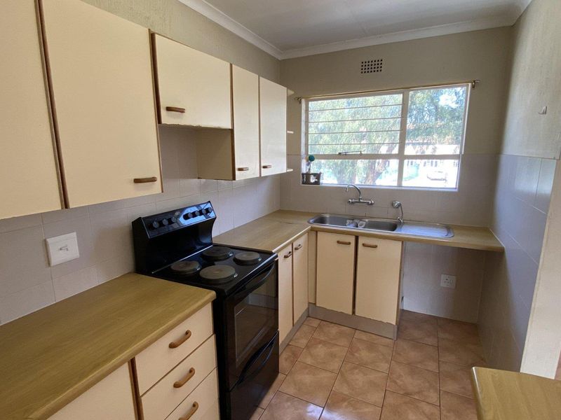 A functional kitchen featuring laminate countertops, built-in cabinetry, a stainless steel double sink, and a freestanding electric stove with tiled flooring and backsplash.