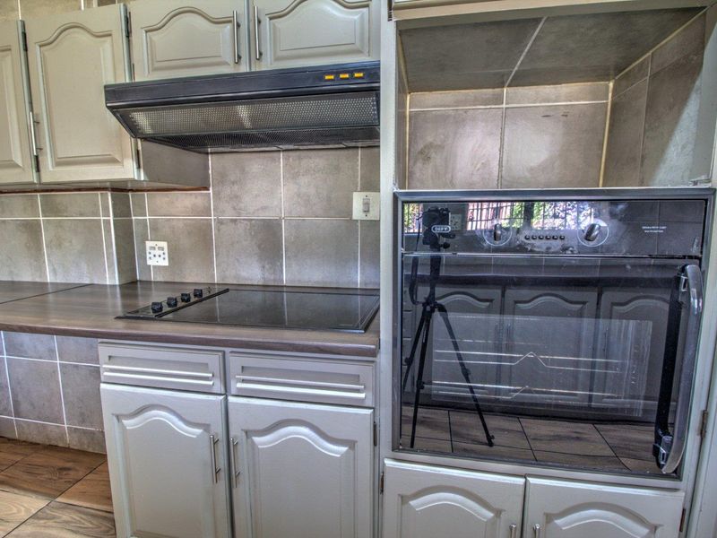 A functional kitchen featuring built-in cabinetry, a laminate countertop, a ceramic tile backsplash, and integrated cooking appliances including an oven and hob.