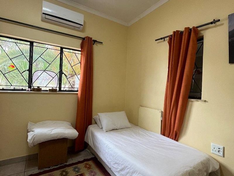 A functional bedroom featuring tiled flooring, a wall-mounted air conditioning unit, and security bars on the windows.