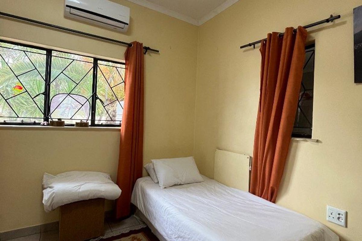 A functional bedroom featuring tiled flooring, a wall-mounted air conditioning unit, and security bars on the windows.