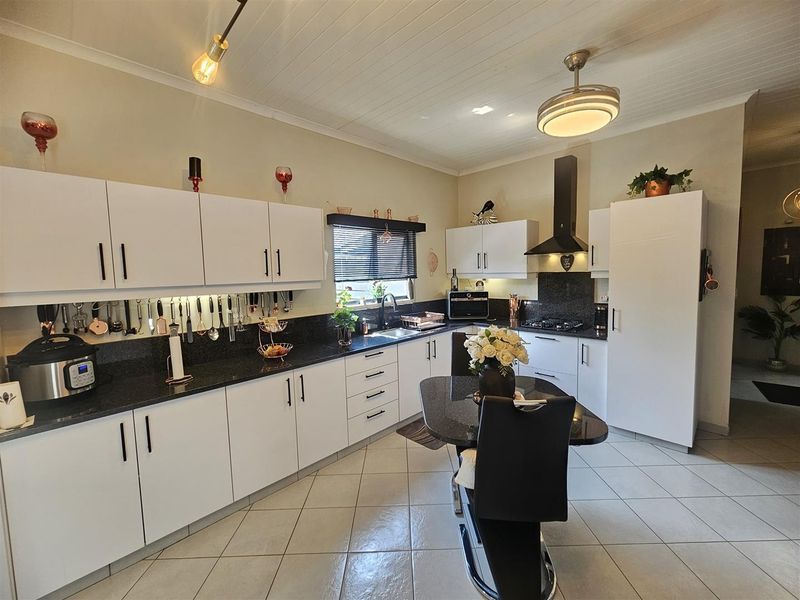 A well-maintained kitchen featuring white cabinetry, dark granite countertops, a gas hob with extractor fan, and tiled flooring.