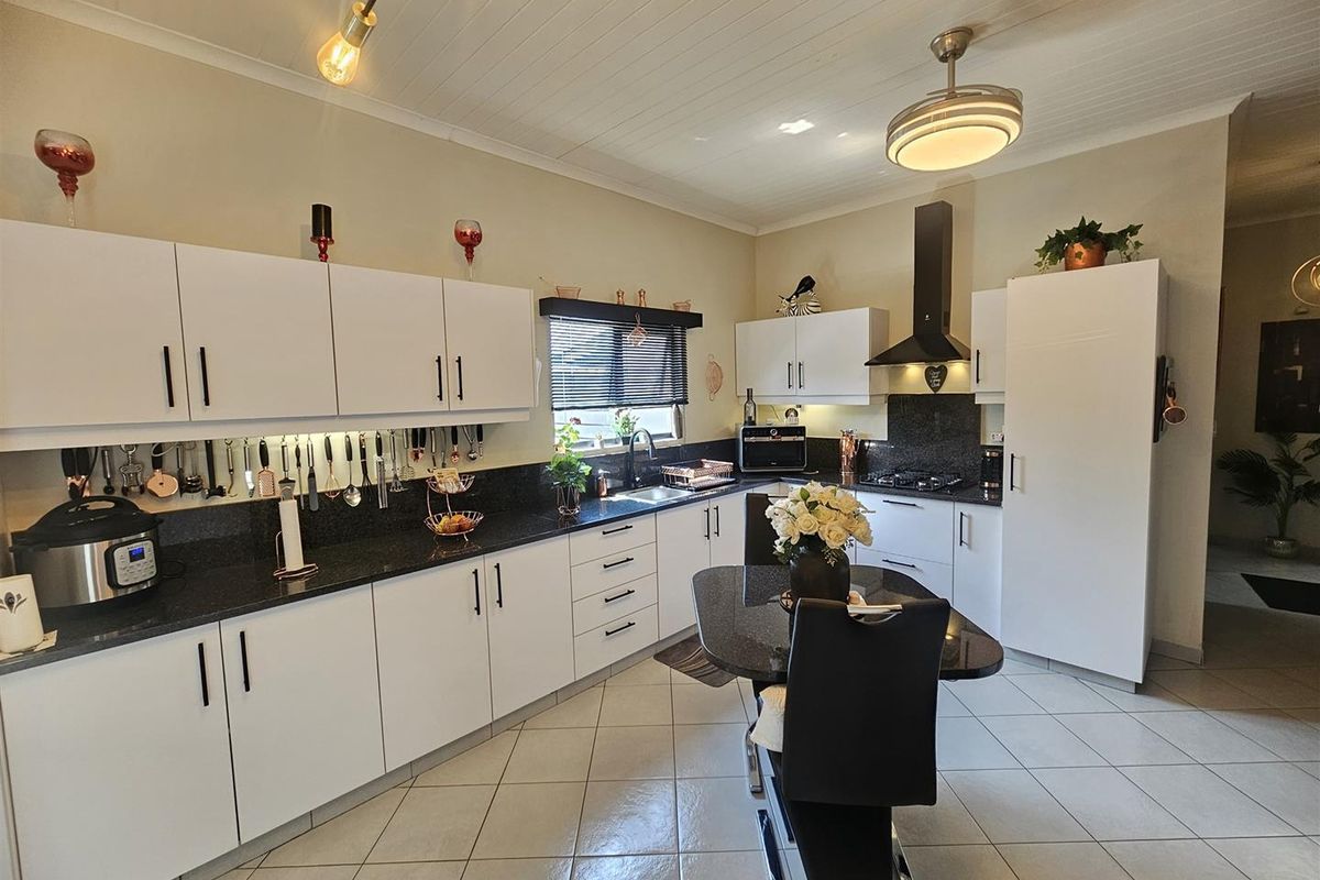 A well-maintained kitchen featuring white cabinetry, dark granite countertops, a gas hob with extractor fan, and tiled flooring.