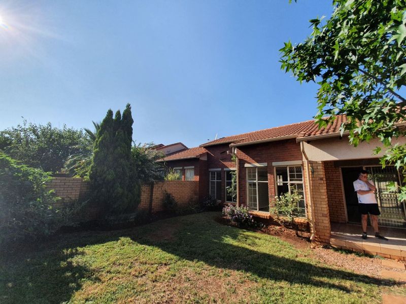 A rear view of the townhouse featuring a brick facade, tiled roof, and a small private garden with a covered patio area.