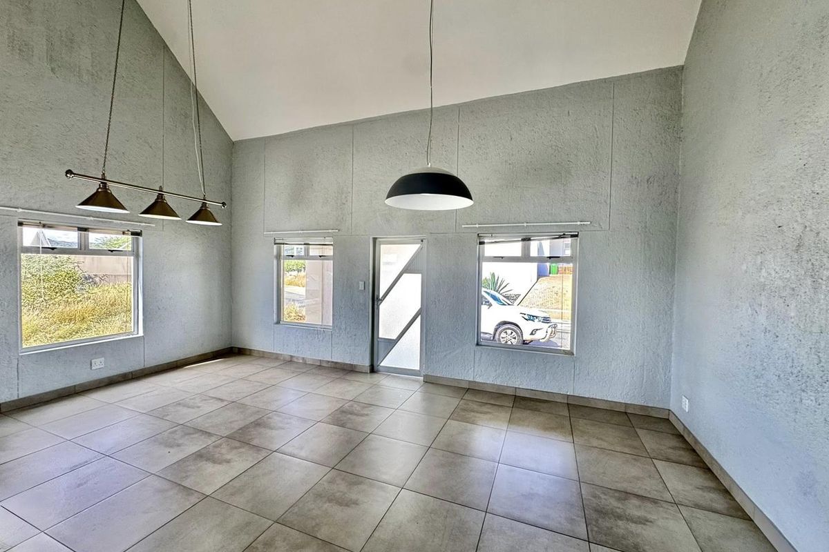 Spacious living area featuring high vaulted ceilings, large windows for natural light, and neutral tiled flooring throughout.