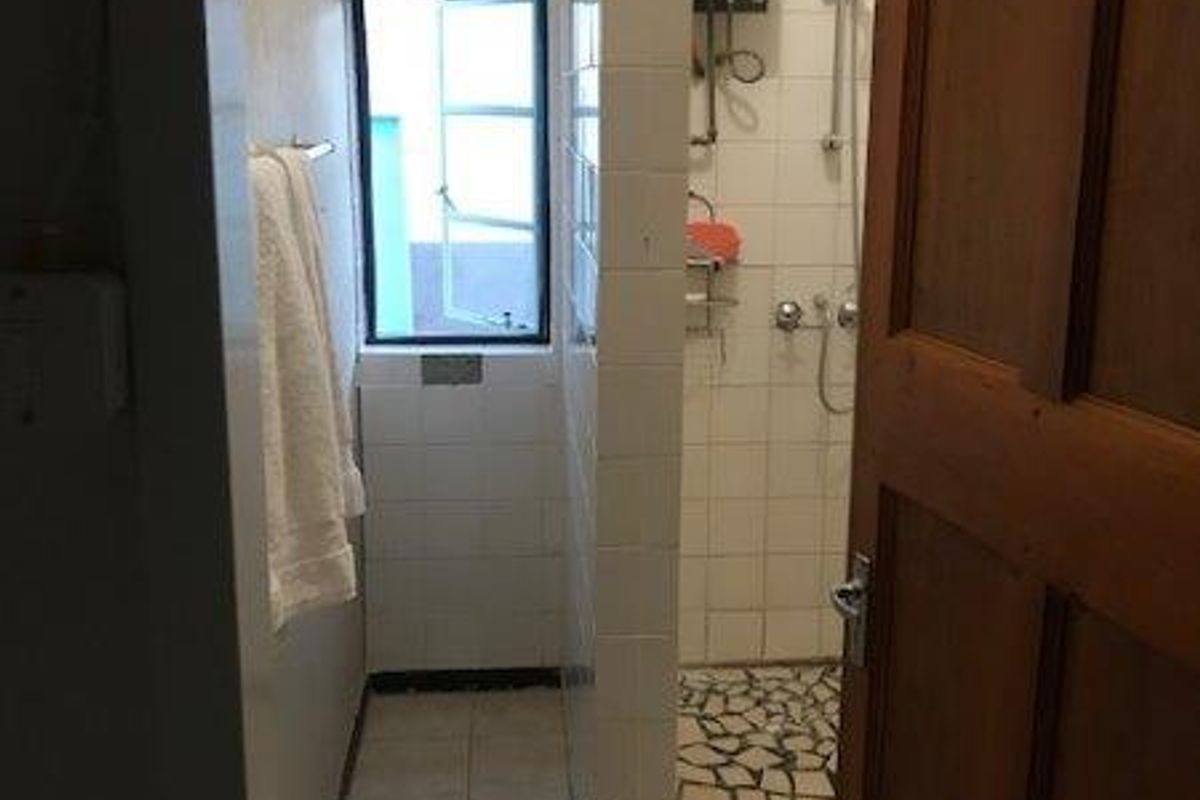A functional bathroom featuring a walk-in shower enclosure with tiled flooring, wall-mounted gas geyser, and a window for natural ventilation.