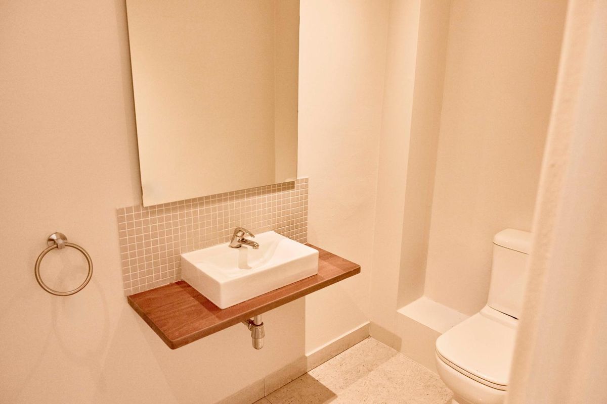 A compact office restroom featuring a wall-mounted timber vanity, vessel sink, mosaic tile backsplash, and a modern toilet.