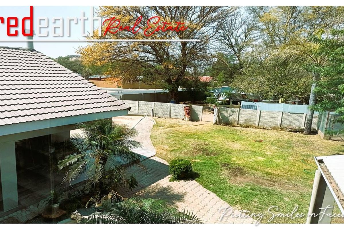 A view of the rear garden featuring a paved walkway, established trees, and a perimeter boundary wall.