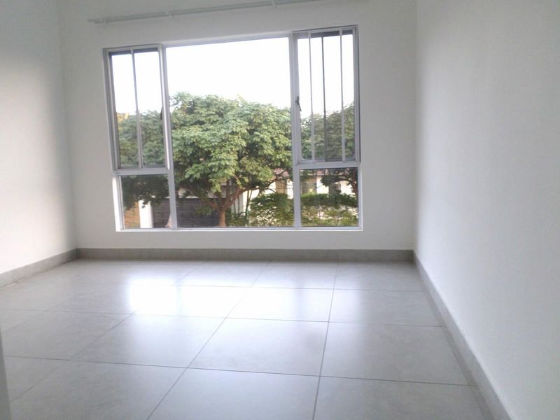 A bright, empty bedroom featuring neutral tiled flooring and large aluminium-framed windows with security bars, offering a clean and versatile living space.