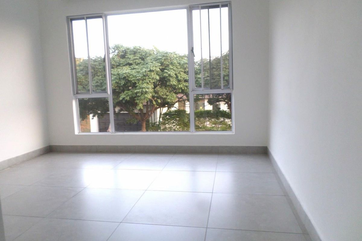 A bright, empty bedroom featuring neutral tiled flooring and large aluminium-framed windows with security bars, offering a clean and versatile living space.