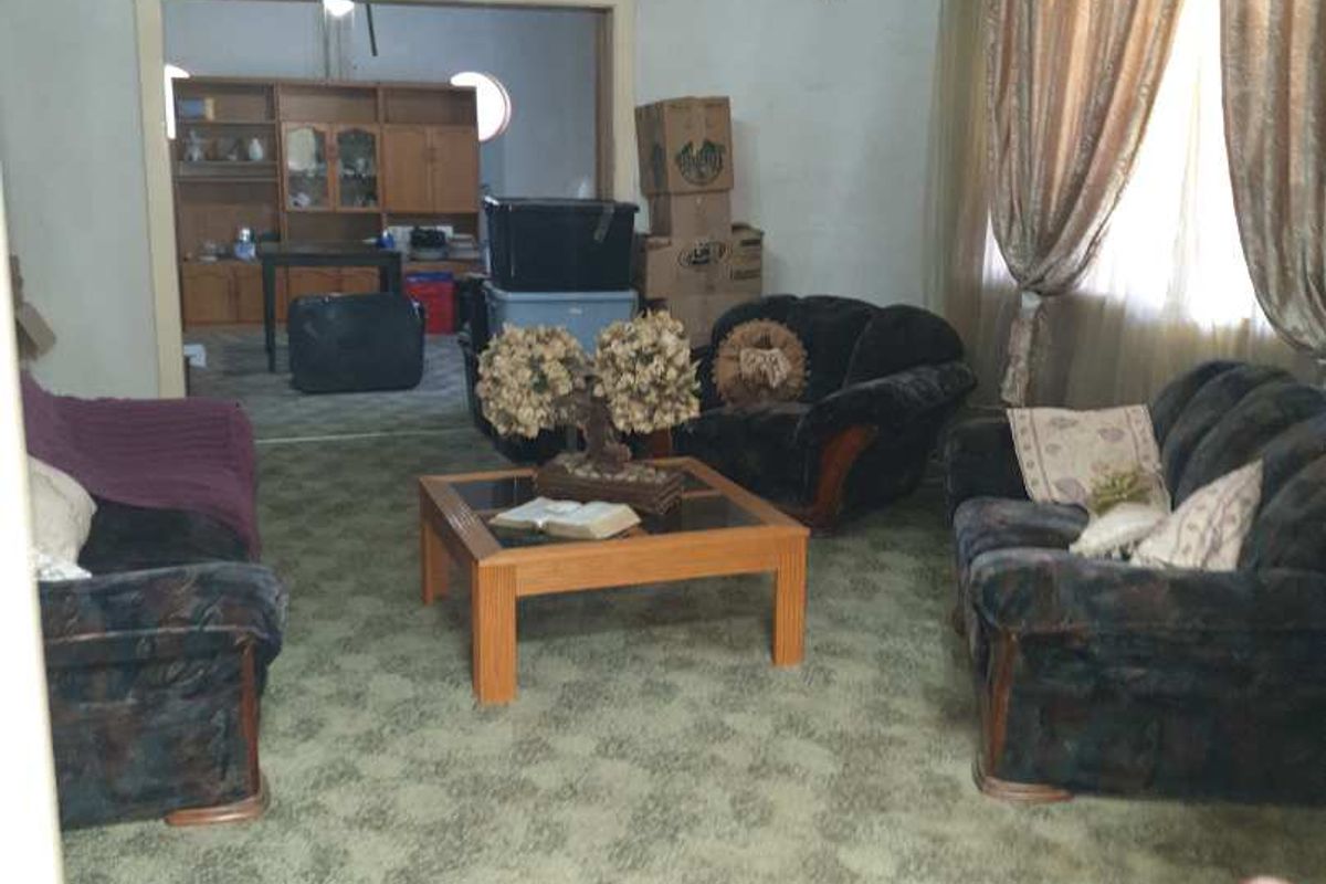 A living room featuring patterned wall-to-wall carpeting and a central chandelier, with an open transition into an adjacent dining or utility area.