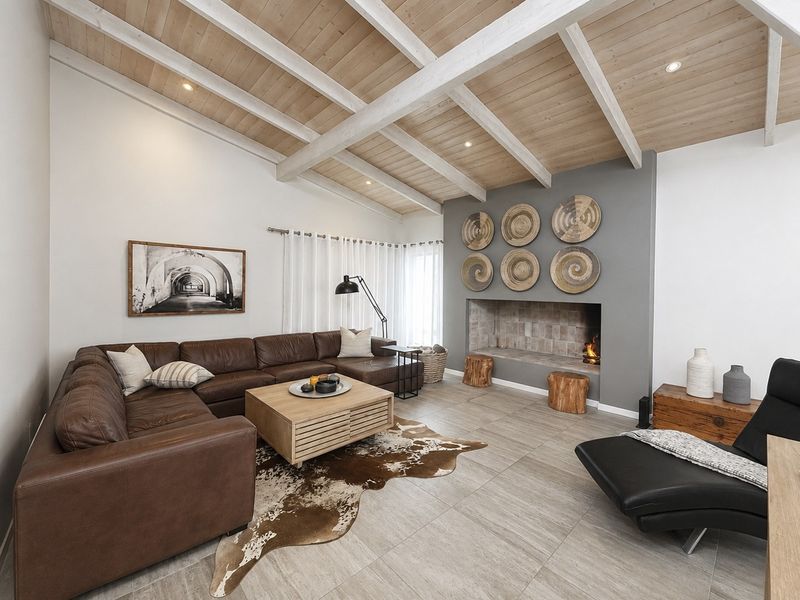 Spacious living room featuring a vaulted timber ceiling with exposed beams, tiled flooring, and a prominent built-in fireplace as a central focal point.