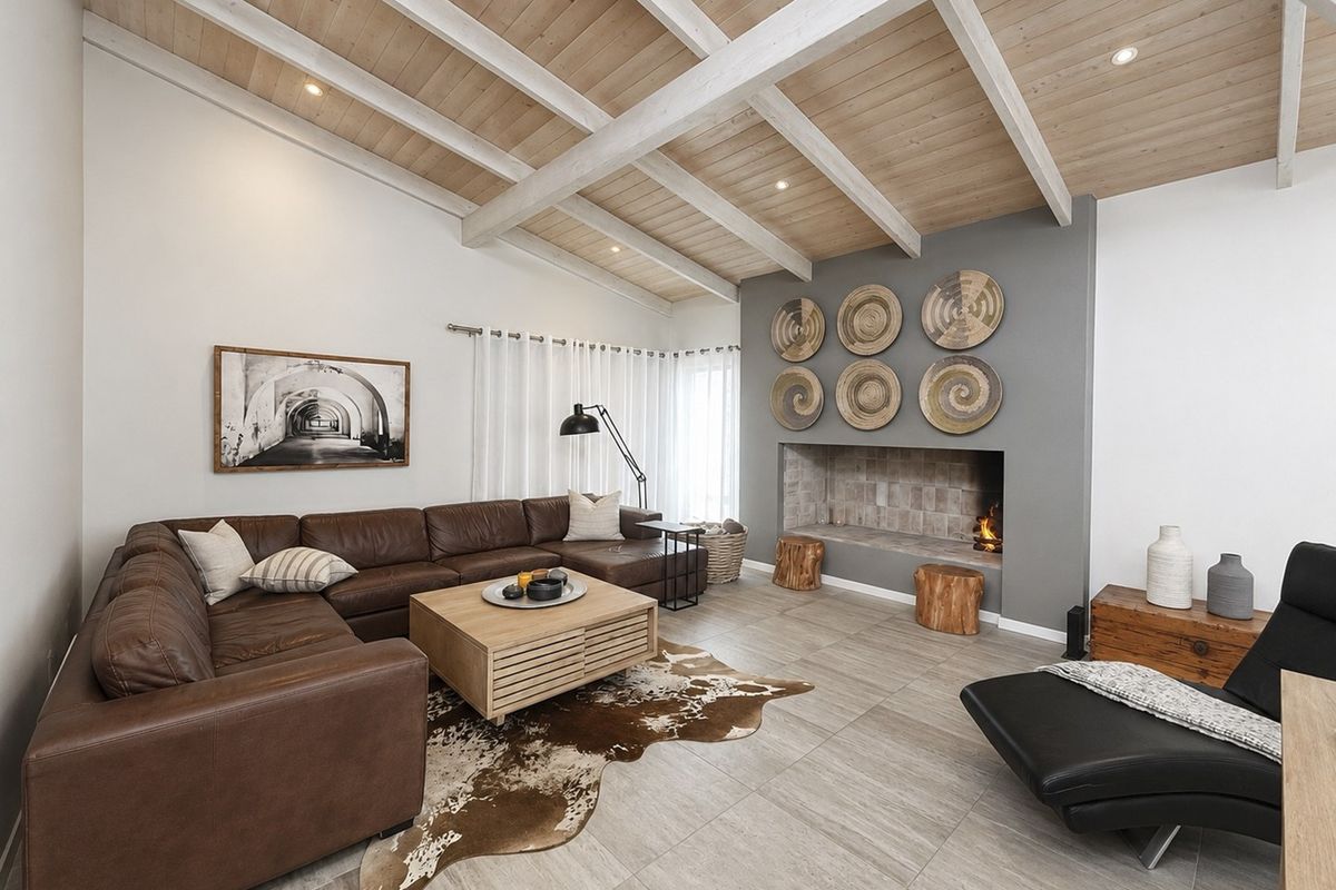Spacious living room featuring a vaulted timber ceiling with exposed beams, tiled flooring, and a prominent built-in fireplace as a central focal point.