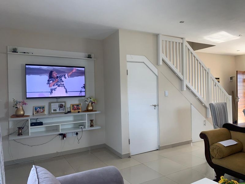 A well-maintained living room featuring a built-in media unit, tiled flooring, and a staircase with a white wooden balustrade.