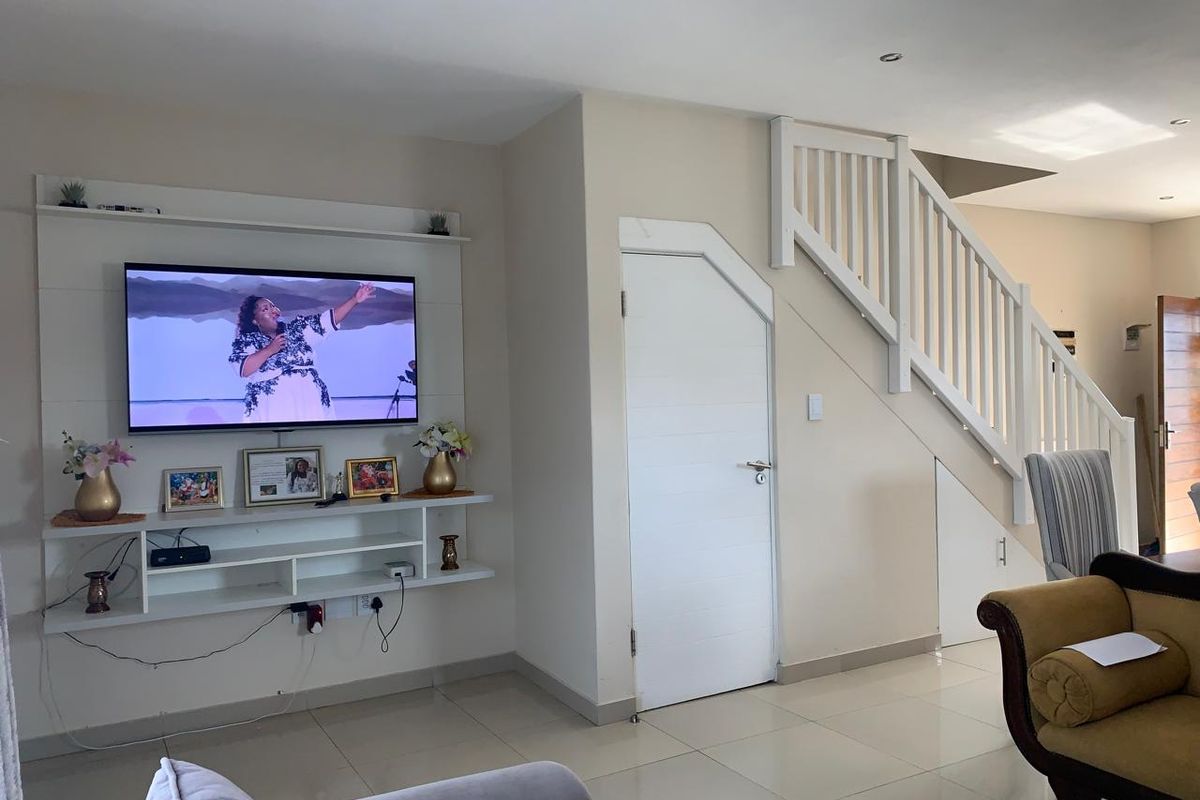 A well-maintained living room featuring a built-in media unit, tiled flooring, and a staircase with a white wooden balustrade.