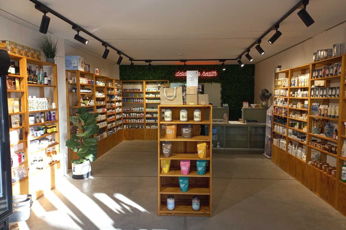 A well-maintained retail space featuring extensive built-in wooden shelving, modern track lighting, a service counter, and a decorative artificial green wall.