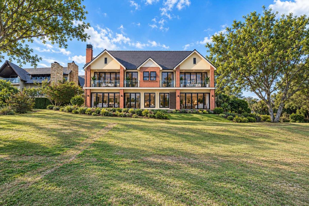 A stunning rear view of a luxury two-story residence featuring a brick facade, expansive glass doors, and a beautifully maintained garden.