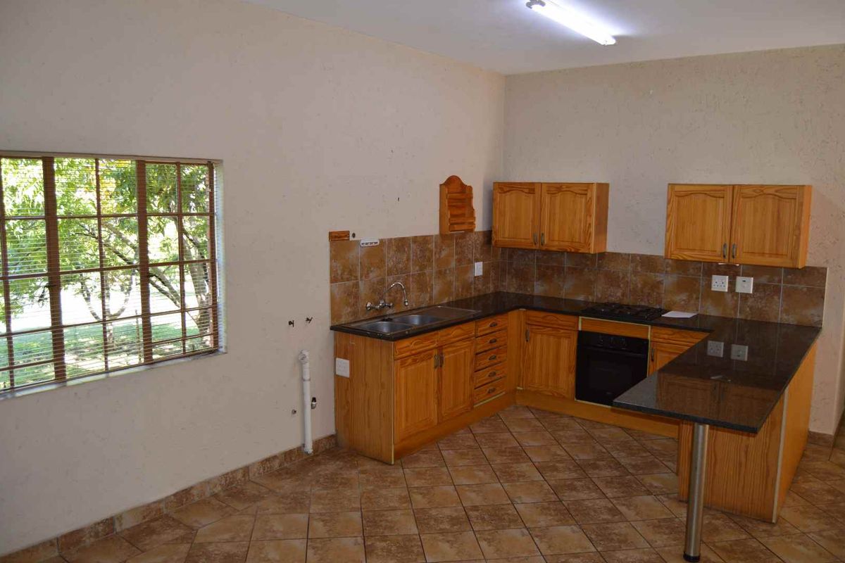 A functional kitchen featuring wooden cabinetry, dark granite countertops, a built-in oven and hob, and tiled flooring with a large window.