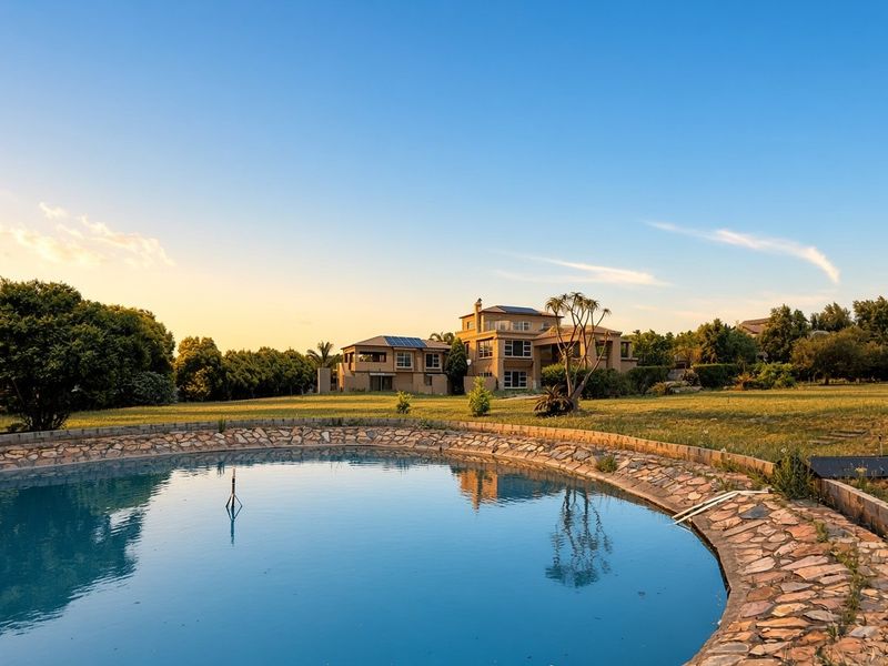 A wide-angle view of a large swimming pool with stone-clad coping, set within a spacious garden overlooking the main residence.