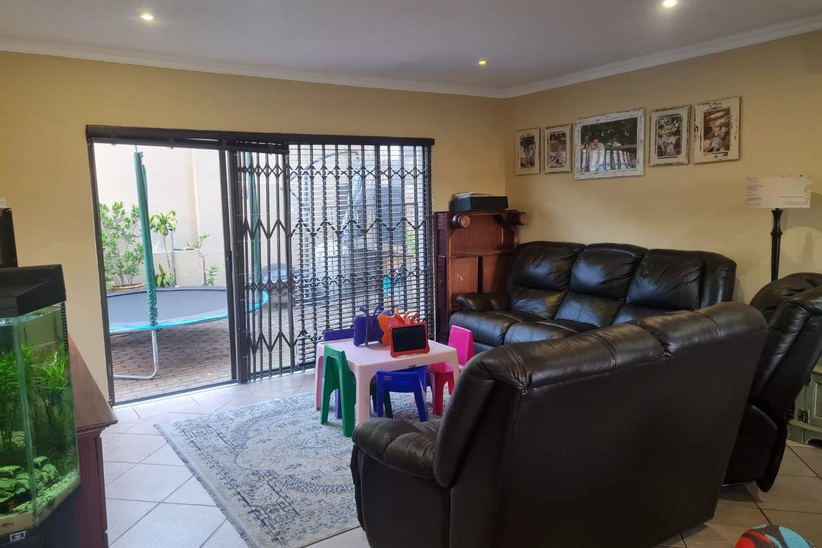 Spacious living room featuring tiled flooring, recessed downlighting, and large sliding glass doors with security gates providing direct access to the outdoor patio area.