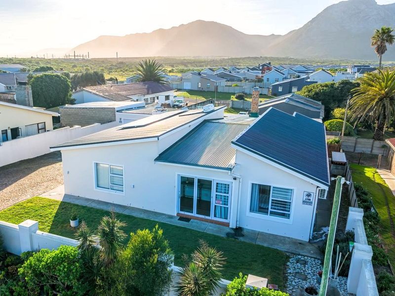 Aerial view of a well-maintained residential property featuring a modern metal roof, solar panels, and a private garden with mountain views.