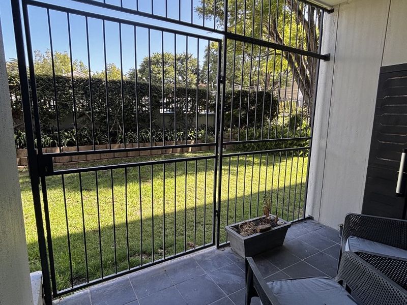 A covered patio area featuring dark floor tiles and a secure metal gate leading out to a private garden space.