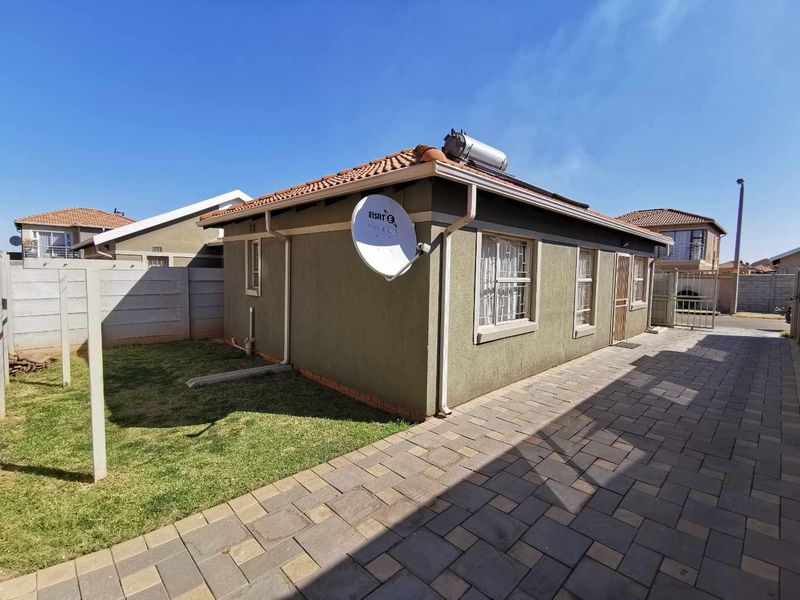 Rear exterior view of the house featuring a paved side area, small lawn, solar water heating system, and security bars on windows.