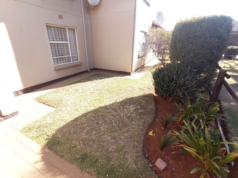 A rear exterior view of the townhouse featuring a small paved patio area, a patch of lawn, and established garden beds with timber fencing.