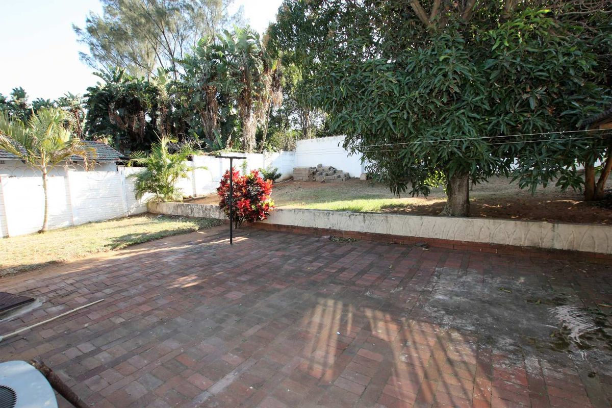 Rear garden area featuring a brick paved patio, retaining wall, and perimeter boundary wall with established trees.