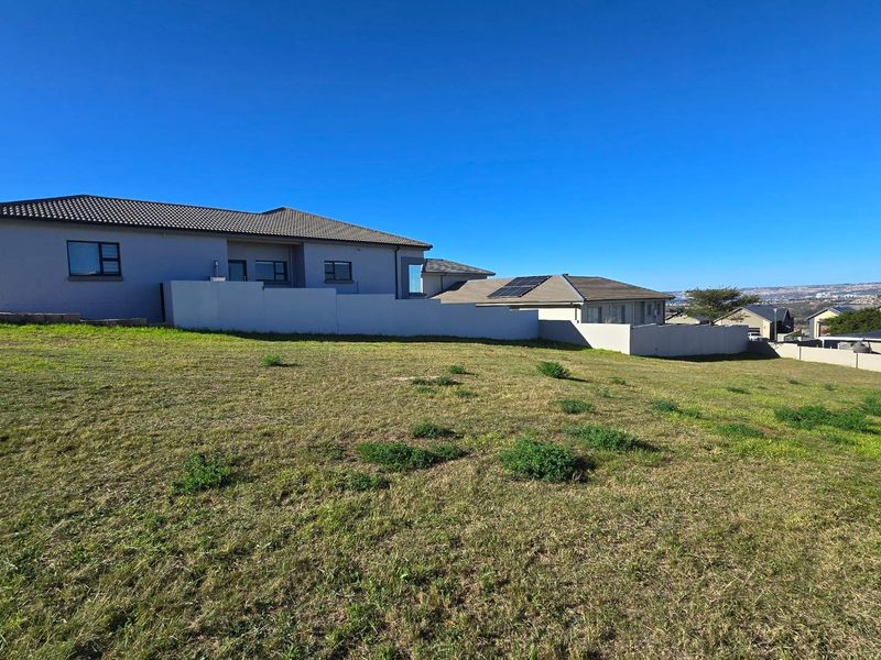 A view of a vacant residential plot featuring a gentle slope, established boundary walls, and surrounding suburban residential properties.