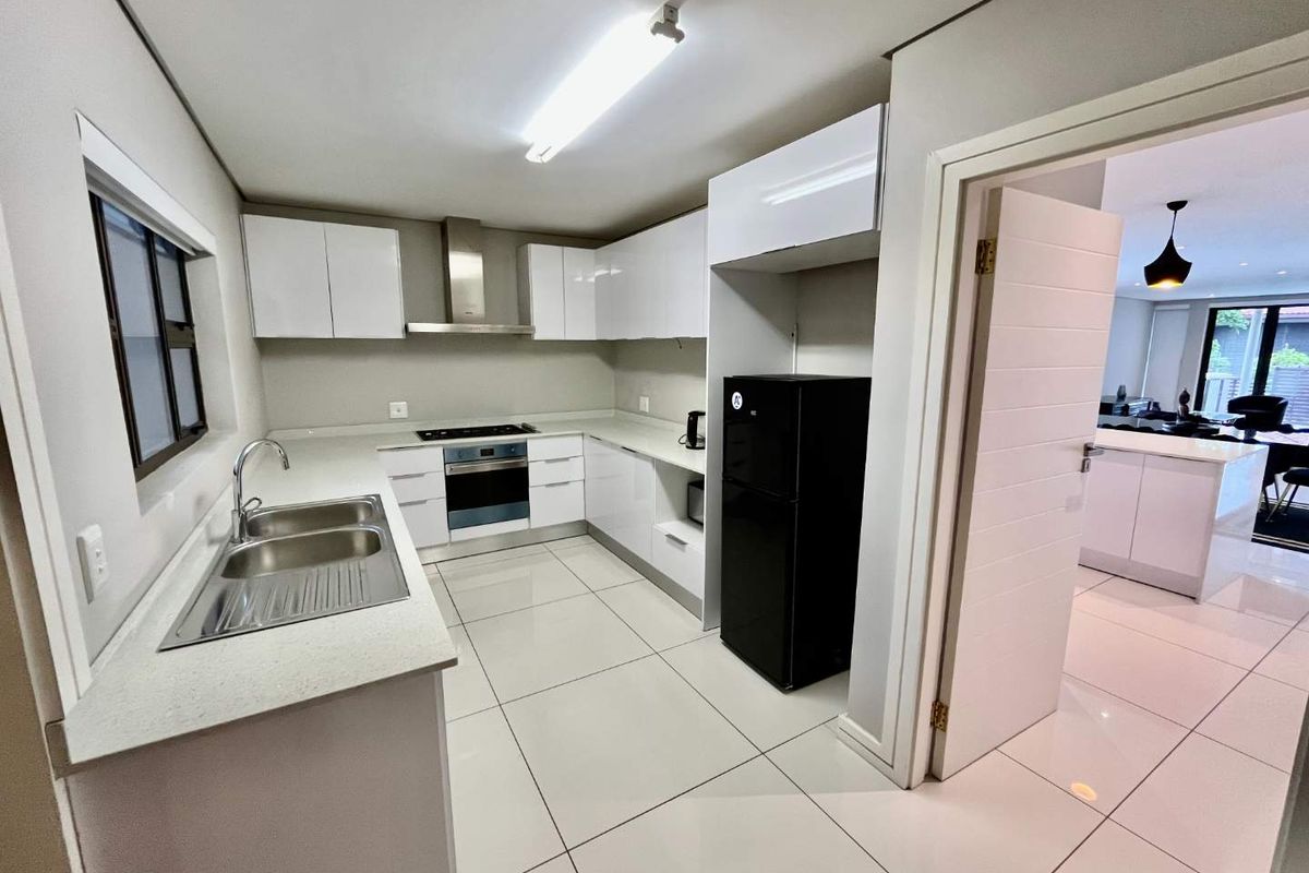 Modern kitchen featuring white high-gloss cabinetry, stone countertops, stainless steel sink, built-in oven, and hob with extractor fan, finished with large format floor tiles.