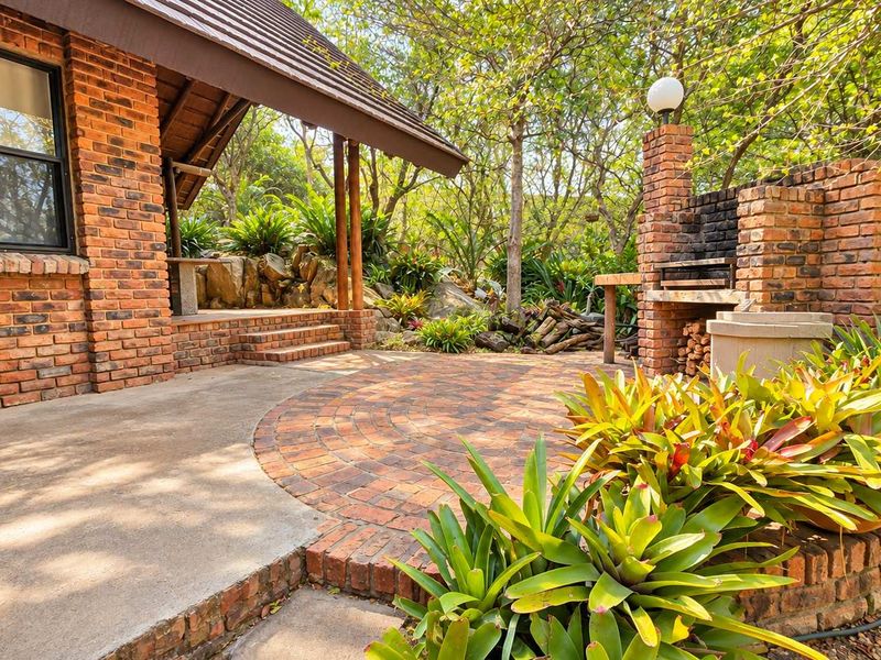 A charming outdoor patio area featuring a built-in brick braai, decorative brick paving, and a covered veranda overlooking a landscaped garden.
