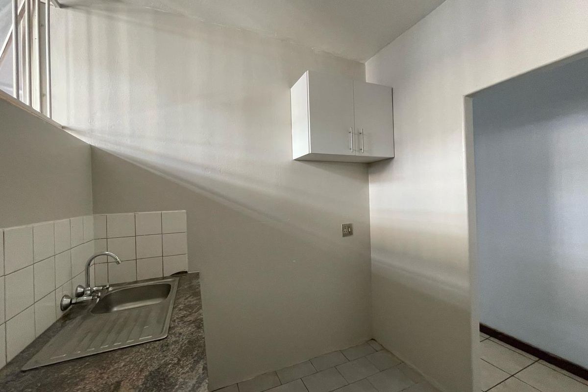 A functional kitchen area featuring a stainless steel sink, tiled splashback, laminate countertop, and a wall-mounted storage cabinet.
