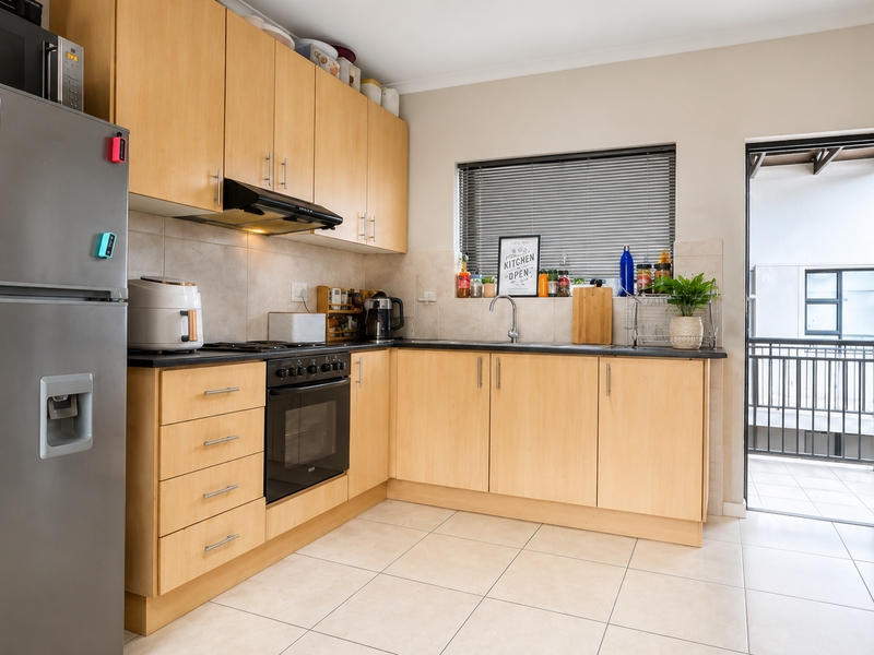 Functional kitchen featuring light wood cabinetry, built-in oven, extractor fan, and tiled flooring, with direct access to an outdoor balcony area.
