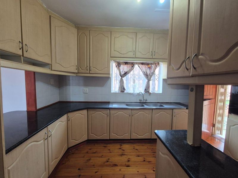 A functional kitchen featuring light-toned cabinetry, dark granite countertops, a double stainless steel sink, and warm timber flooring.