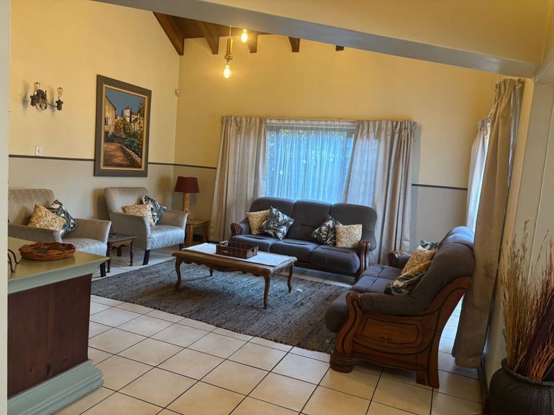 Spacious living room featuring a vaulted ceiling with exposed timber beams and neutral ceramic floor tiles.