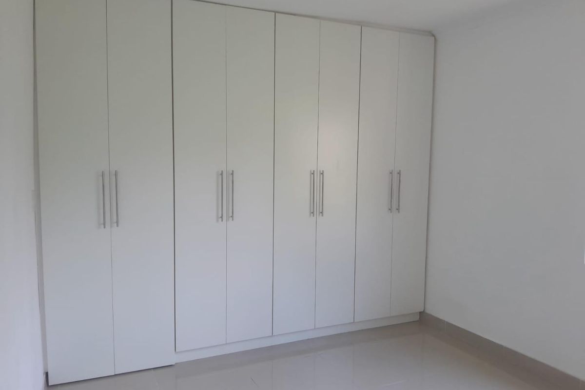 A clean, empty bedroom featuring modern white built-in cupboards and neutral tiled flooring, offering a blank canvas for personalization.