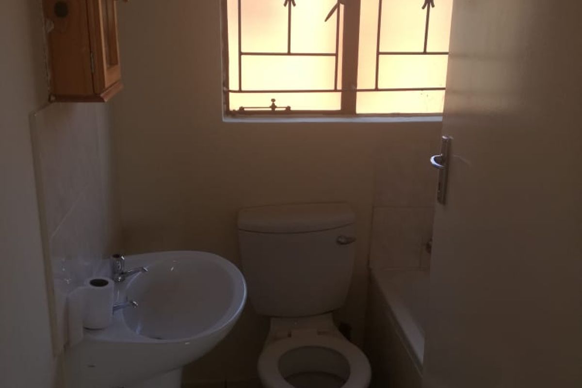 A functional bathroom featuring a pedestal basin, toilet, and bathtub, with security bars on the window.