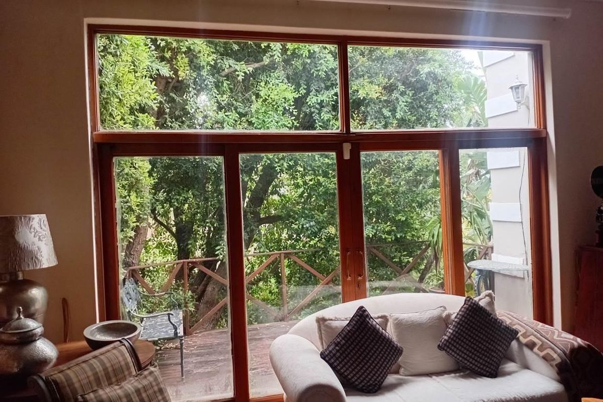 A living room featuring large timber-framed windows and sliding doors that provide a view of the outdoor deck and garden area.