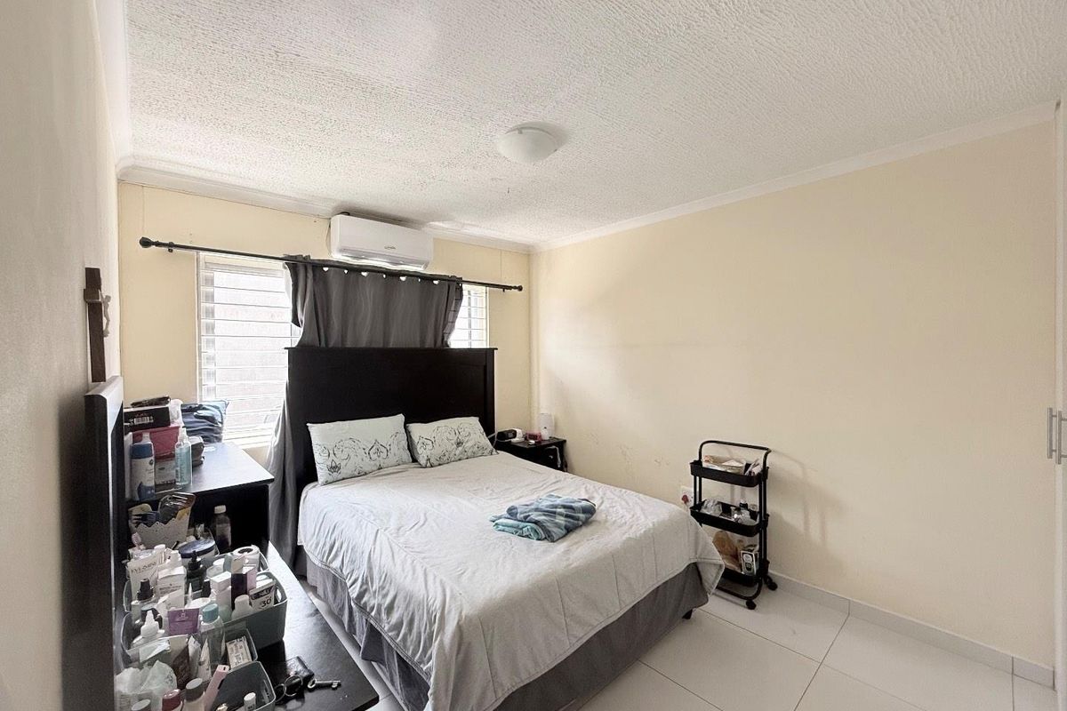 A bedroom featuring tiled flooring, a wall-mounted air conditioning unit, and louvered windows, providing a functional and comfortable sleeping space.