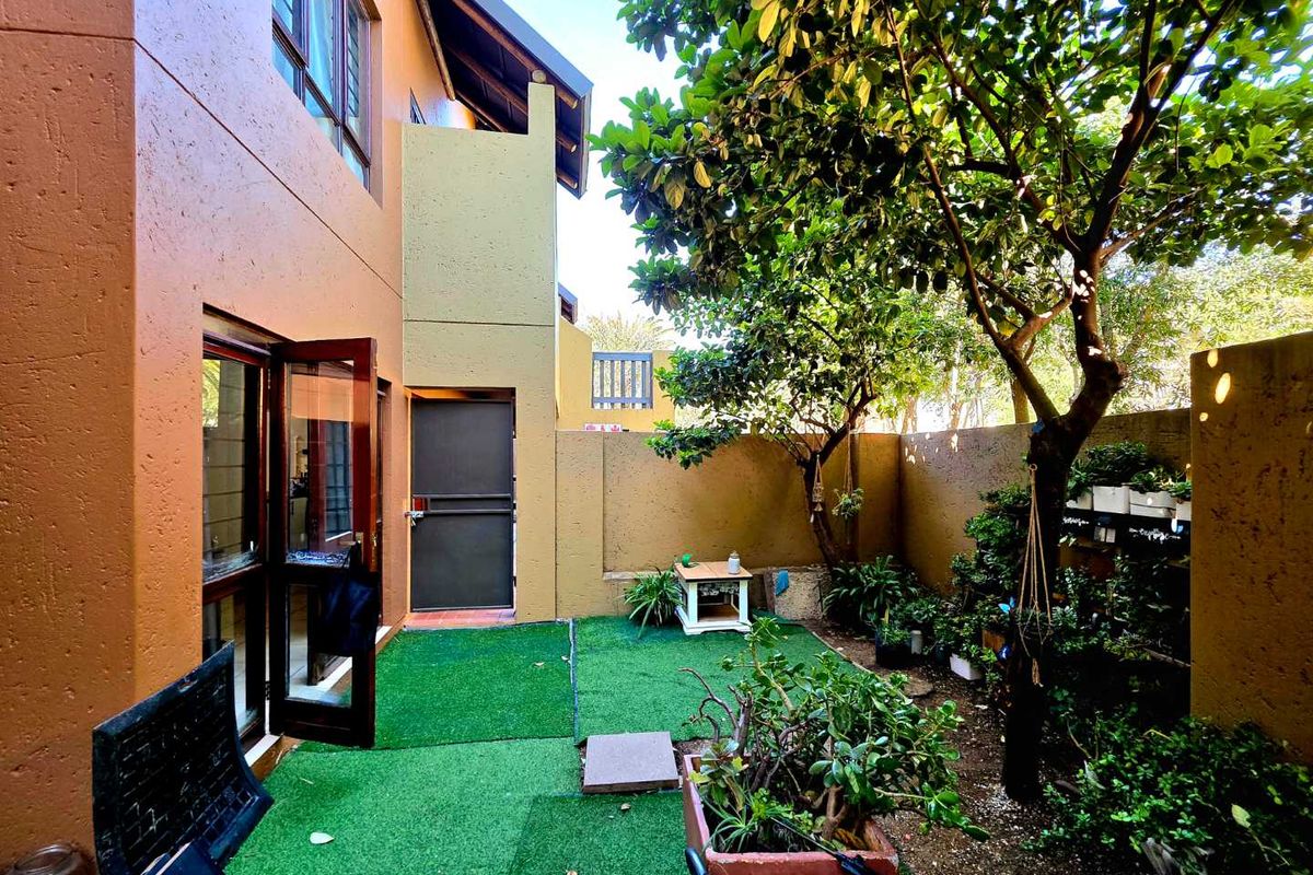 A private rear courtyard featuring artificial turf, established trees, and direct access to the apartment through a security door and casement windows.