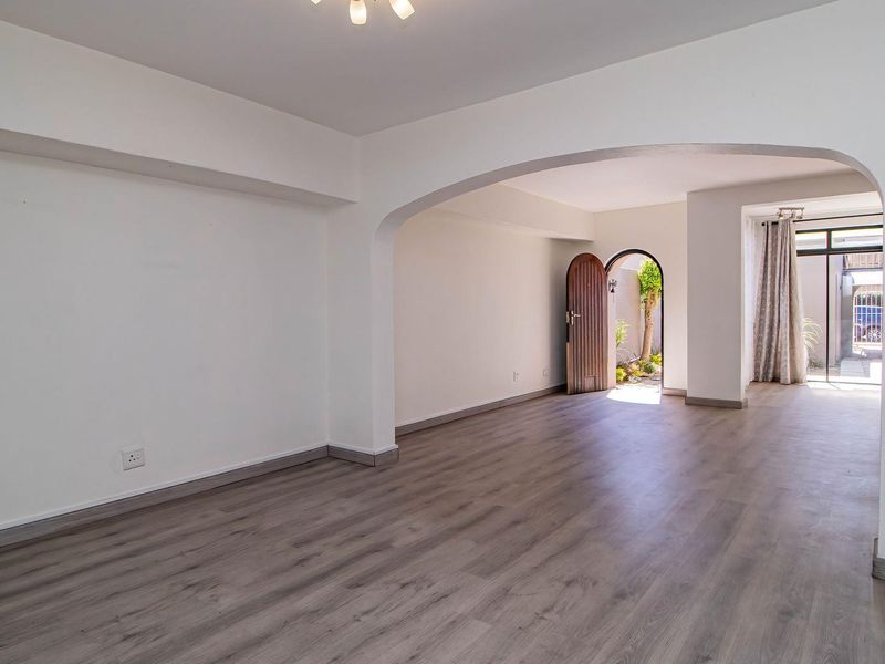 A bright, open-plan living area featuring modern laminate flooring, neutral walls, and an elegant arched transition leading to an outdoor space.