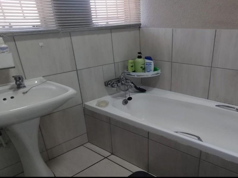 A functional bathroom featuring a pedestal basin, a standard bathtub with mixer tap, and neutral wall and floor tiling.