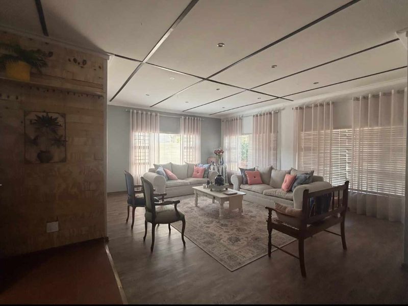 Spacious living room featuring laminate flooring, a distinctive panelled ceiling with recessed lighting, and large windows allowing for ample natural light.