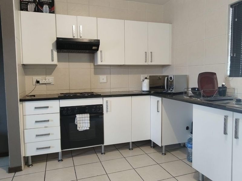 A functional kitchen featuring white cabinetry, black granite countertops, a built-in oven with hob, and tiled splashbacks.
