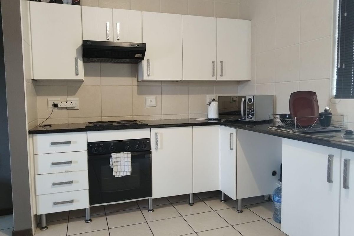 A functional kitchen featuring white cabinetry, black granite countertops, a built-in oven with hob, and tiled splashbacks.