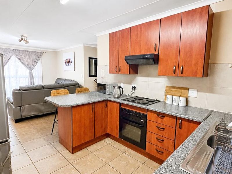 Open-plan kitchen and living area featuring wood-finish cabinetry, granite countertops, built-in oven, and ceramic floor tiles throughout.